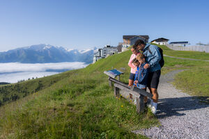 Familie betrachtet eine Infotafel, im Hintergrund ist die Bergstationd der Schmittenhöhebahn zu sehen | © Mr. Offenblende