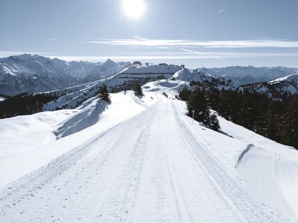 Snowy mountain path with distant peaks under the sun. | © Alpine Vision