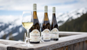 Three bottles of white wine and a glass on a wooden table in the mountains. | © Nikolaus Faistauer Photography