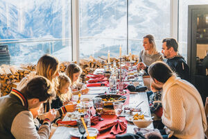 Ein festlich gedeckter Tisch in der AreitAlm mit Gästen, die gemeinsam essen und den Alpenblick genießen. | © Schmittenhöhebahn AG/umundauf.at