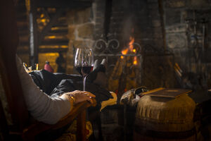 Eine Person genießt Rotwein am Kamin in der Blaickner's Sonnalm. | © Schmittenhöhebahn AG/Max Steinbauer