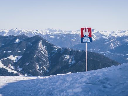 Ein Warnschild mit Stop Handzeichen auf einem Bergpfad, umgeben von schneebedeckten Bergen. | © Stefanie Oberhauser