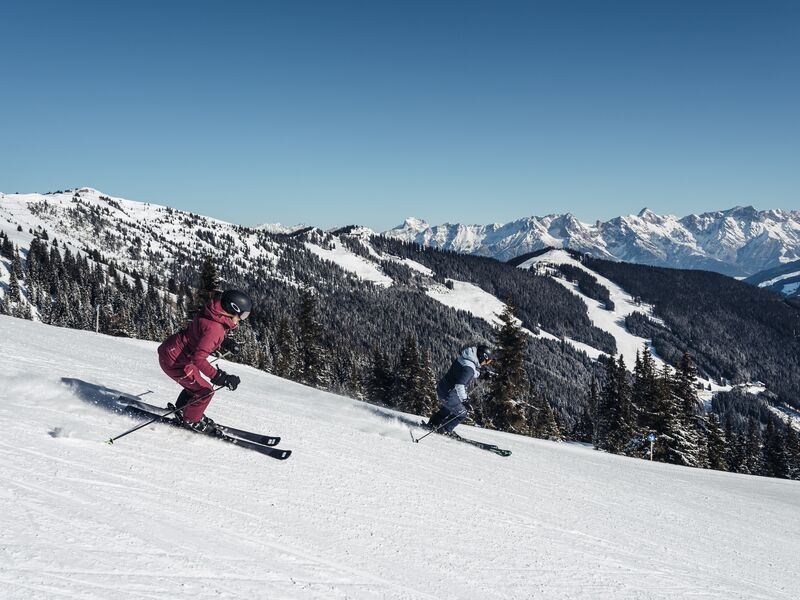 Skifahren in der verschneiten Berglandschaft | © Korbinian Seifert Zwei Skifahrer gleiten über eine schneebedeckte Piste bei klarem Himmel. | © Korbinian Seifert