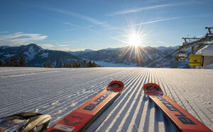 Skis and sunrise on a white, groomed slope. | © Schmittenhöhebahn AG/Nikolaus Faistauer Photography