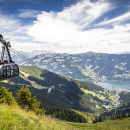 Eine Seilbahn schwebt über grüne Hänge. | © Schmittenhöhebahn AG/Max Steinbauer