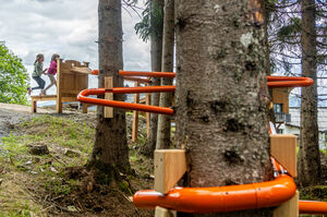 Children exploring a play structure with orange pipes in the forest. | © Gerald Lobenwein