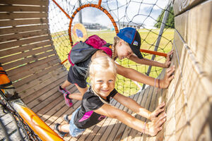 Two children playing and smiling in a wooden play structure. | © Max Steinbauer