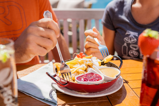 Zwei Personen essen im Bergrestaurant Franzl ein Gericht mit Pommes und Saucen. | © mr-offenblende.at