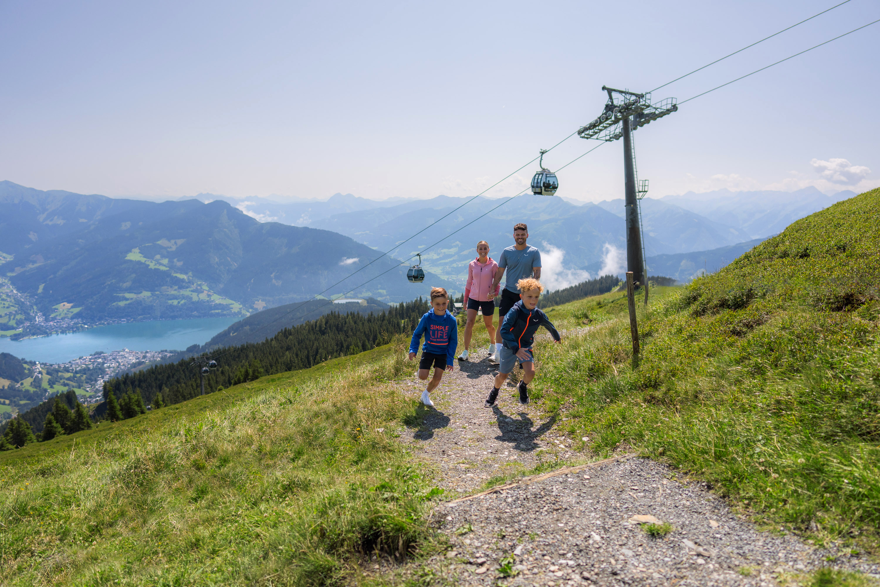 Familie auf einem Wanderweg unter dem trassXpress, die Kinder laufen vor den Eltern. | © Schmittenhöhebahn AG/Mr. Offenblende