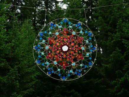 Ein farbenfrohes Mandala aus Wolle hängt zwischen den Bäumen. | © Amina Angelina Nührig