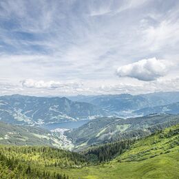 Blick auf grüne Hügel, Berge und einen See unter wolkigem Himmel. | © Schmittenhöhebahn AG/Max Steinbauer
