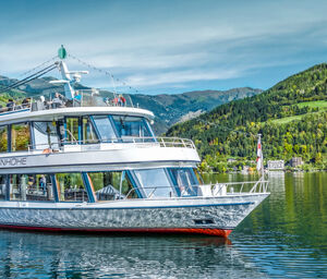 The ship MS Schmittenhöhe sails on a calm lake with green mountains in the background. | © Schmittenhöhebahn AG