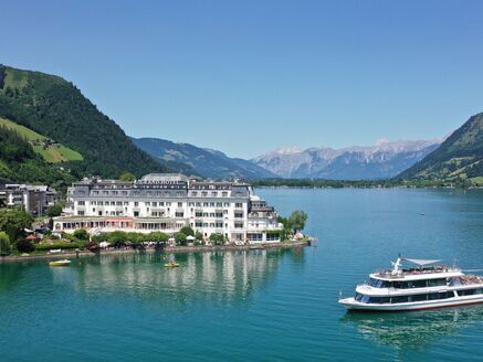 The image shows a picturesque lake with the boat MS Schmittenhöhe and a hotel along the waterfront. | © Schmittenhöhebahn AG