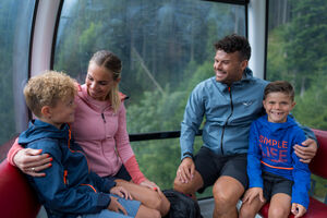Eine Familie lächelt während einer Seilbahnfahrt in den Bergen. | © Schmittenhöhebahn AG/mr-offenblende.at