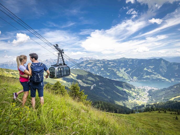 Romantisches Paar auf der Wanderung mit Seilbahn im Hintergrund. | © Schmittenhöhebahn AG/Max Steinbauer