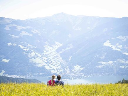 Ein Paar sitzt auf der Höhenpromenade und genießt die Aussicht auf die Berge und den See. | © Schmittenhöhebahn AG/Max Steinbauer