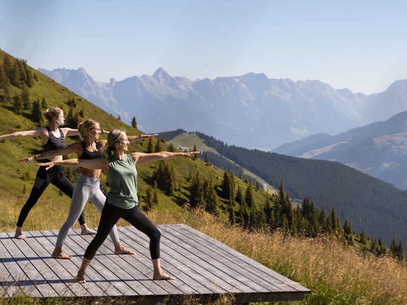 Drei Frauen machen Yoga auf einer Plattform mit Bergblick. | © Kuscheiart