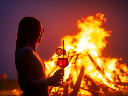 Silhouette einer Person mit Getränk vor großer Feuerstelle. | © Nicola Littmann