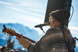 Eine Musikerin spielt Gitarre und singt vor Bergkulisse.