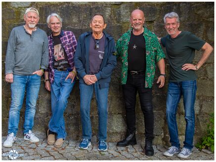 Fünf Männer in Freizeitkleidung, die vor einer Steinmauer stehen.