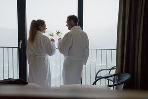 Ein Paar im Bademantel genießt Getränke auf einem Balkon des Berghotel Schmittenhöhe. | © mr-offenblende.at