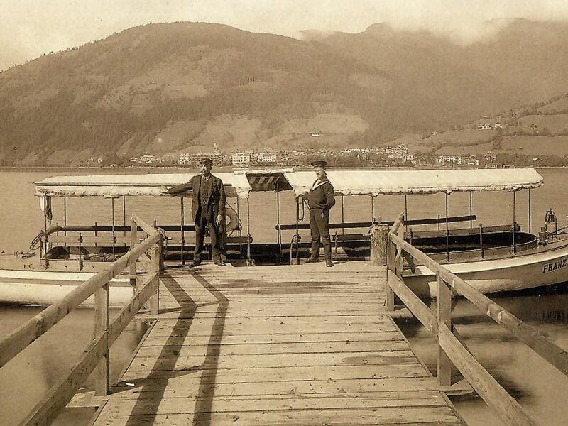 Two men standing next to a boat on Lake Zell, mountains in the background. | © Bezirksarchiv Pinzgau