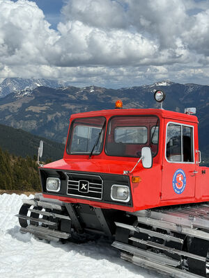 Rote Pistenraupe auf schneebedecktem Berg vor Alpenkulisse.