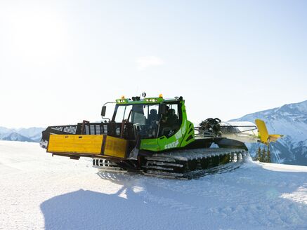 Eine grüne Pistenraupe präpariert den Schnee auf der Schmittenhöhe.