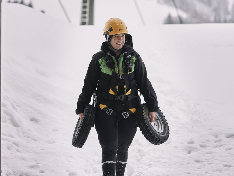 Betriebsleiterin Celina Schuster trägt in Arbeitskleidung Ersatzteile einer Seilbahn durch den Schnee. | © Robert Maybach