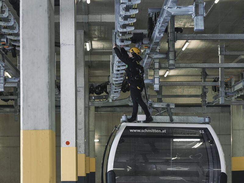 Betriebsleiterin Celina Schuster steht auf einer Gondel der Zell am See Xpress Seilbahn und führt Wartungsarbeiten durch. | © Robert Maybach